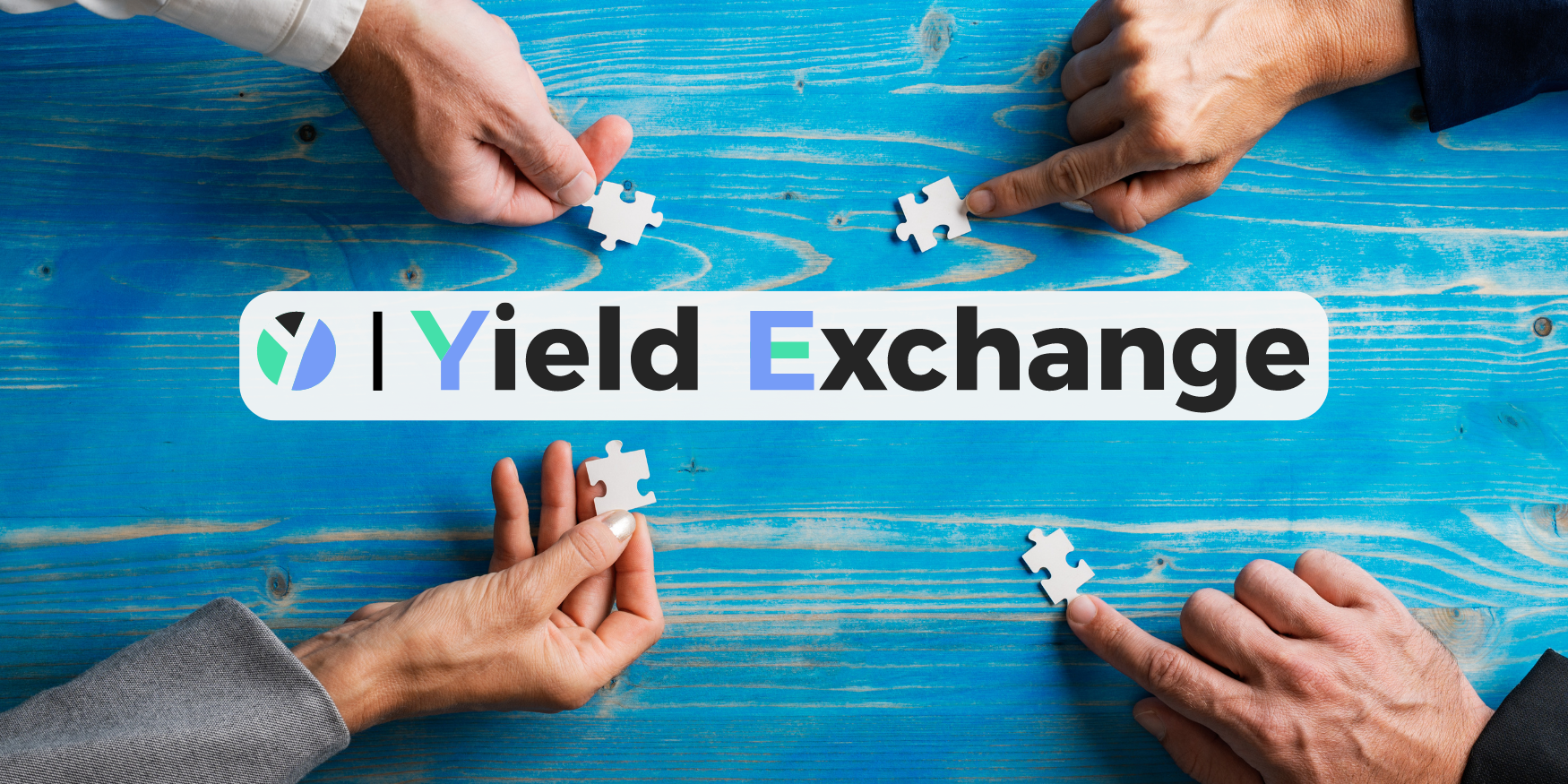 One hand in each corner holding a puzzle piece over a blue table, arms angled towards centre, with the Yield Exchange Logo in the middle.